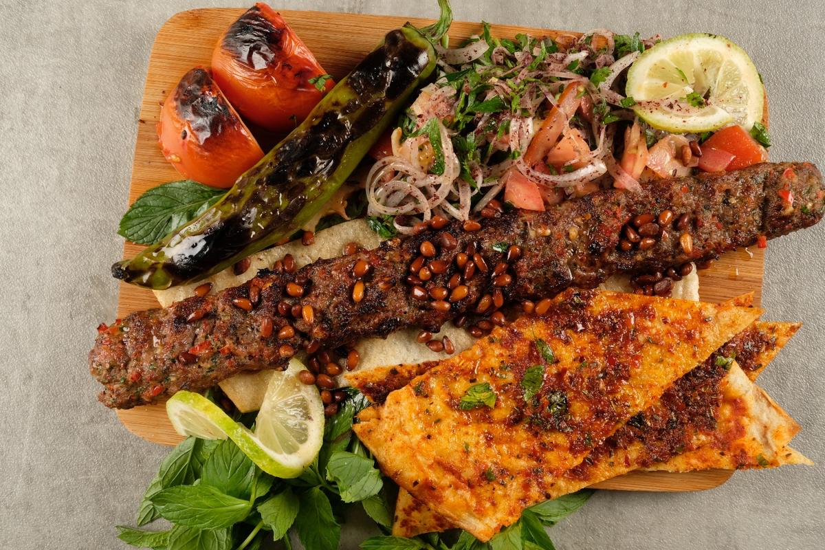 Fıstıklı kebap, közlenmiş biber ve soğan salatasıyla servis