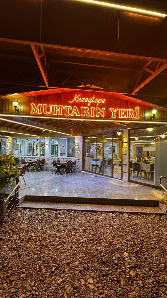 Kuzeytepe Muhtarın Yeri restoranının ışıklı giriş kapısı ve dış terası